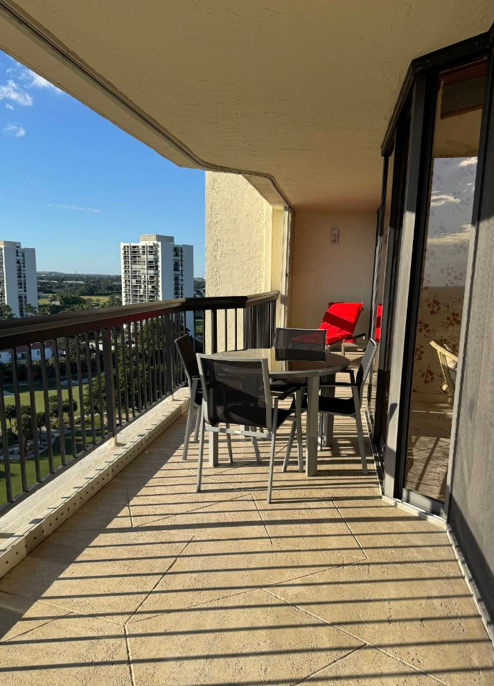 Balcony with a table and chairs, overlooking a golf course and city buildings on a sunny day.