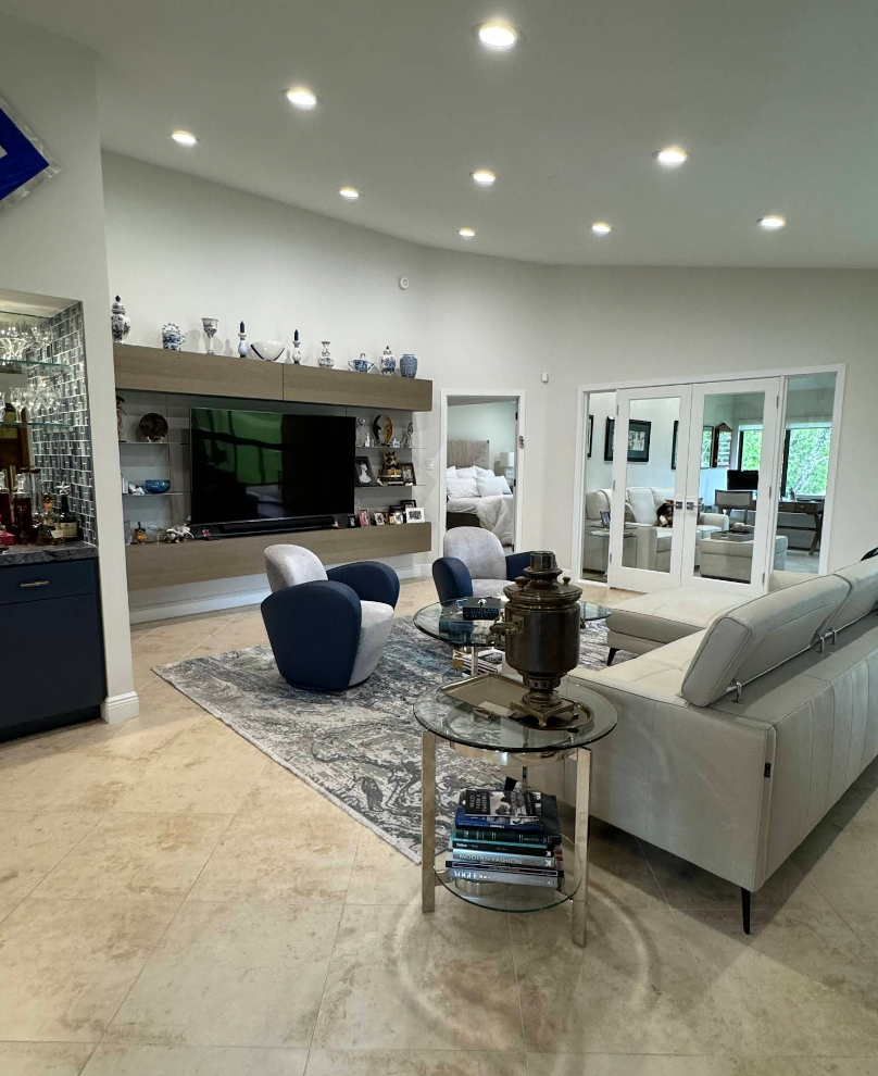 Spacious living room with white walls, TV, blue and white chairs, and glass coffee table.