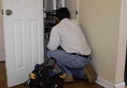 A man is working on a refrigerator in a closet.