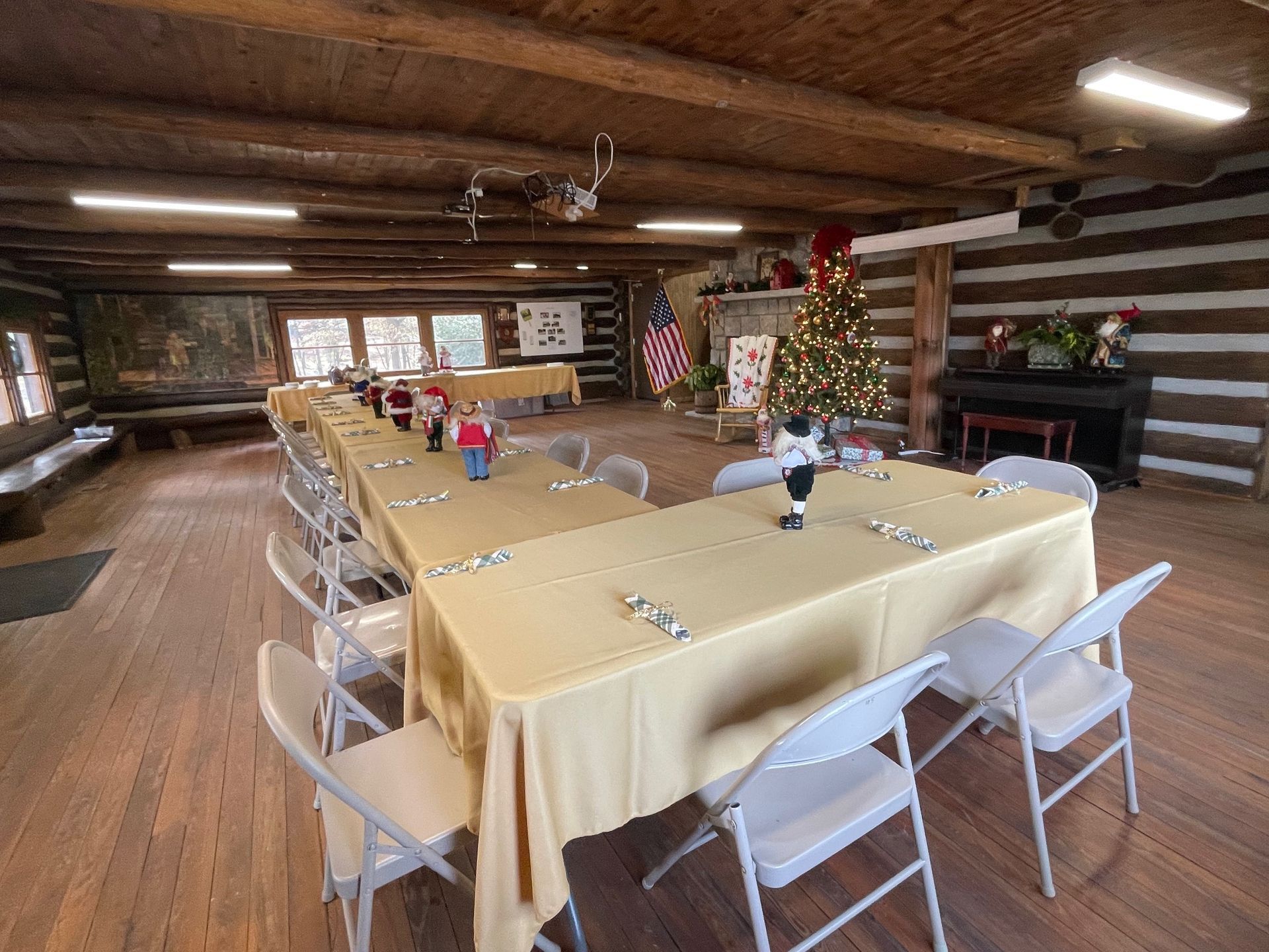 Interior of a log cabin set up for an event with long tables, chairs, and Christmas decorations.