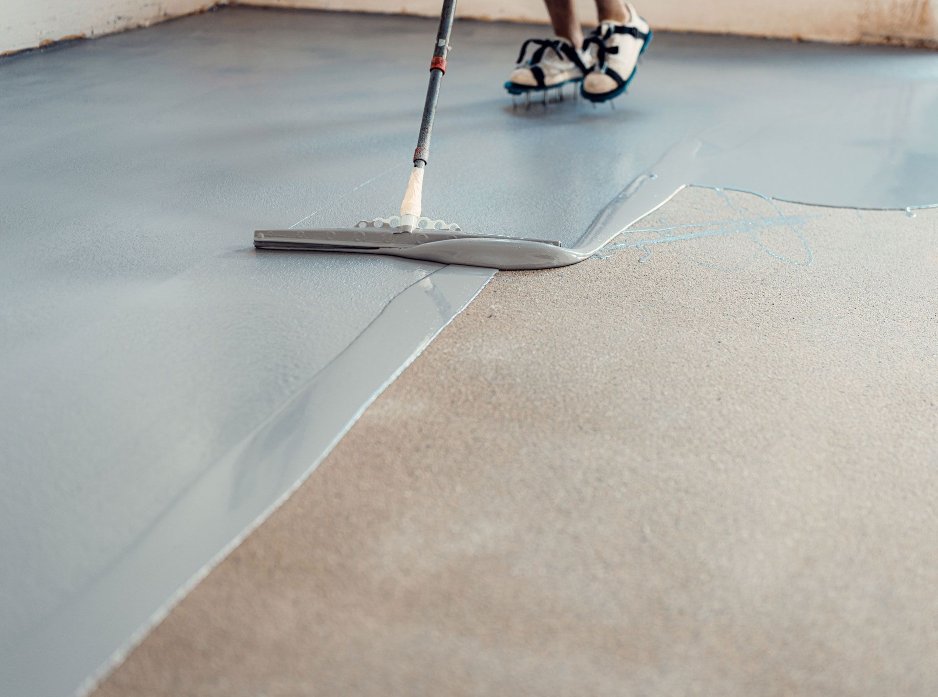 Person applying gray epoxy coating to a concrete floor with a squeegee.
