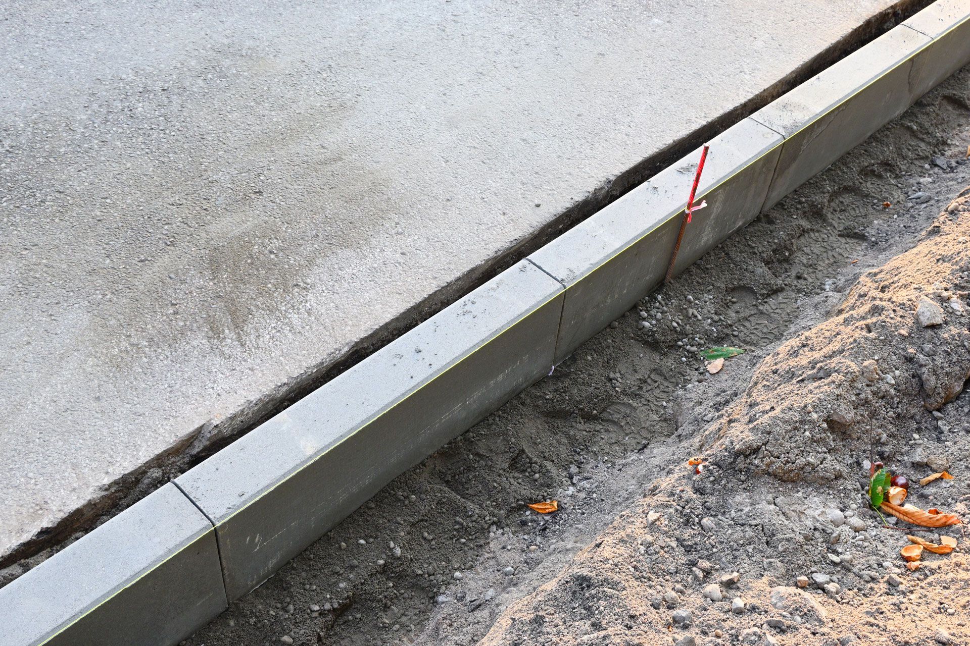 Concrete curb bordering fresh concrete pavement and dirt.