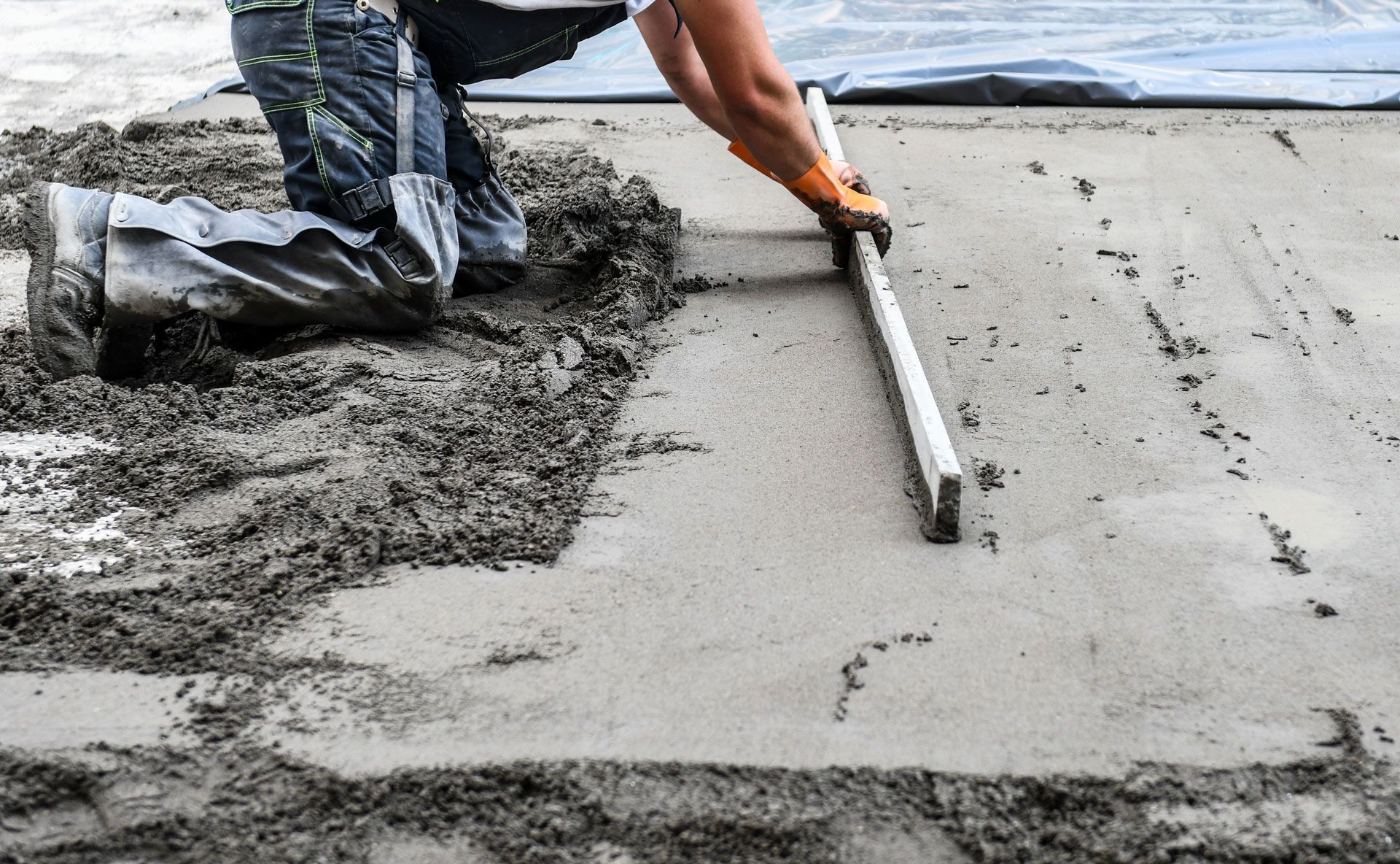 Person leveling wet concrete with a screed; construction site.