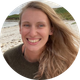 Woman with blonde hair smiling on a beach.