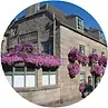 Stone building with pink flower baskets hanging from windows, blue sky.