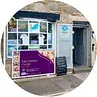 Storefront with purple sign, shirts in window, and open door.