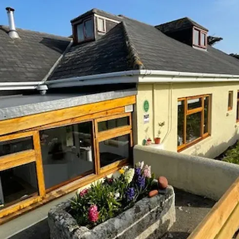 Yellow building with slate roof, dormers, and a flower bed. Sunny day.