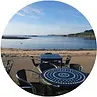 Tables and chairs overlook a beach and calm water under a bright sky.