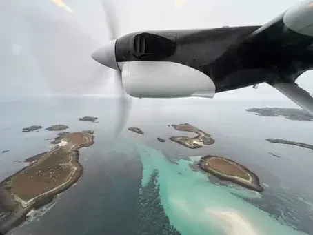 View from a small plane flying over islands and turquoise water under an overcast sky.