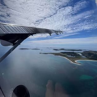 Airplane wing view of a blue sea, islands, and a partly cloudy sky.