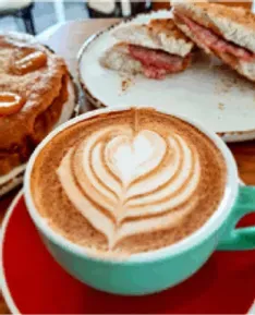 Cappuccino with latte art in a green mug, with food in background.
