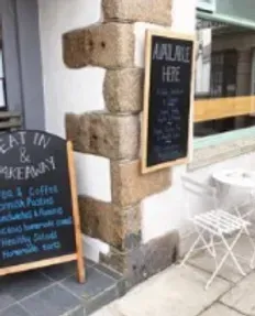 Blackboard signs outside a cafe on a stone pillar, one saying "Available Here," other "Eat in & Takeaway."
