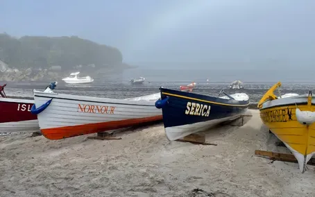 Colorful rowboats on a sandy beach, with a foggy coastline in the background.