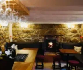 Cozy pub interior with stone walls, fireplace, tables, and hanging wine glasses.
