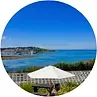 Bright blue sky over ocean, white umbrella over a table, coastal view.