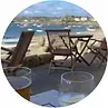 Outdoor cafe with view of boats on a bay; chairs and tables set up, glasses on table.