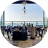 Restaurant interior with tables, ocean view through windows, and hanging light fixtures.