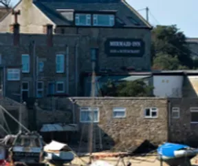 Mermaid Inn pub and restaurant, stone buildings, boats in harbor, sunny day.