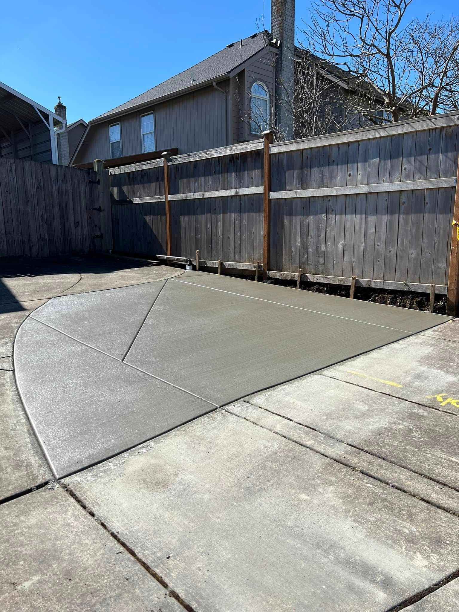 A newly poured, smooth concrete slab section patch integrated into an older, weathered driveway in a suburban backyard.