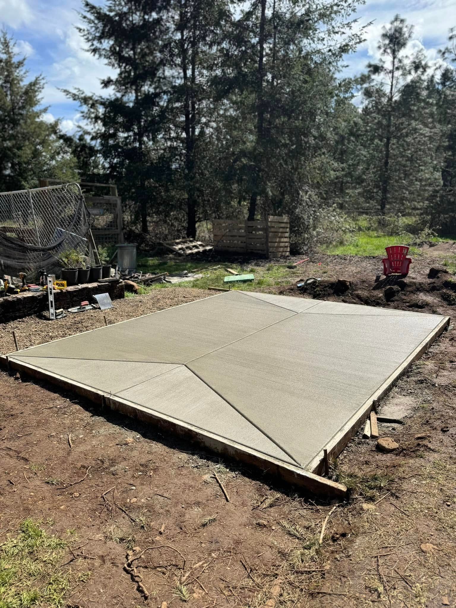 A rectangular concrete slab recently poured in a clearing surrounded by trees, with wooden forms visible at the edges.
