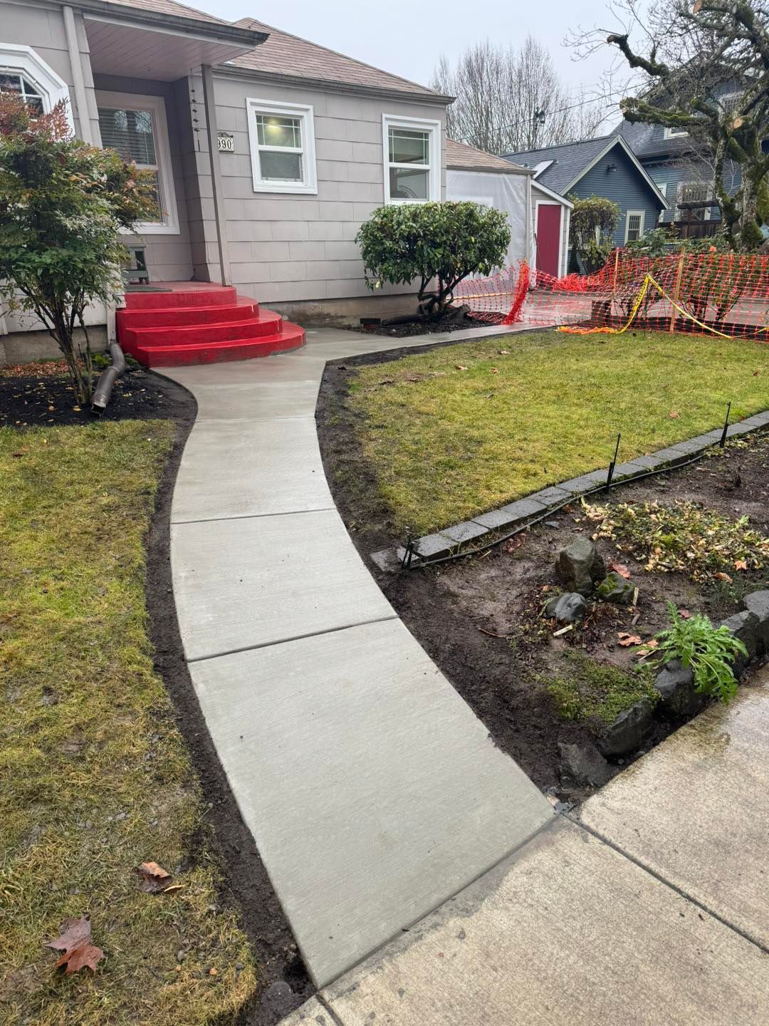 A light gray house with bright red stairs and a newly poured concrete walkway leading to the front entrance.