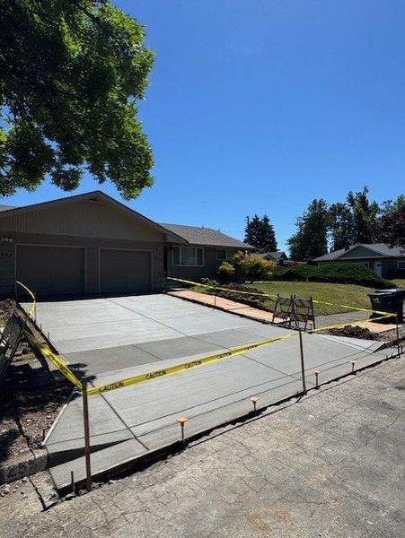 A newly poured concrete driveway leads to the front entrance of a grey, single-story house.
