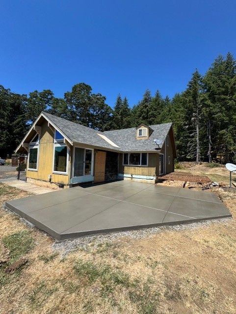 A newly poured concrete patio and steps leading to the entrance of a house under construction wrapped in green siding.