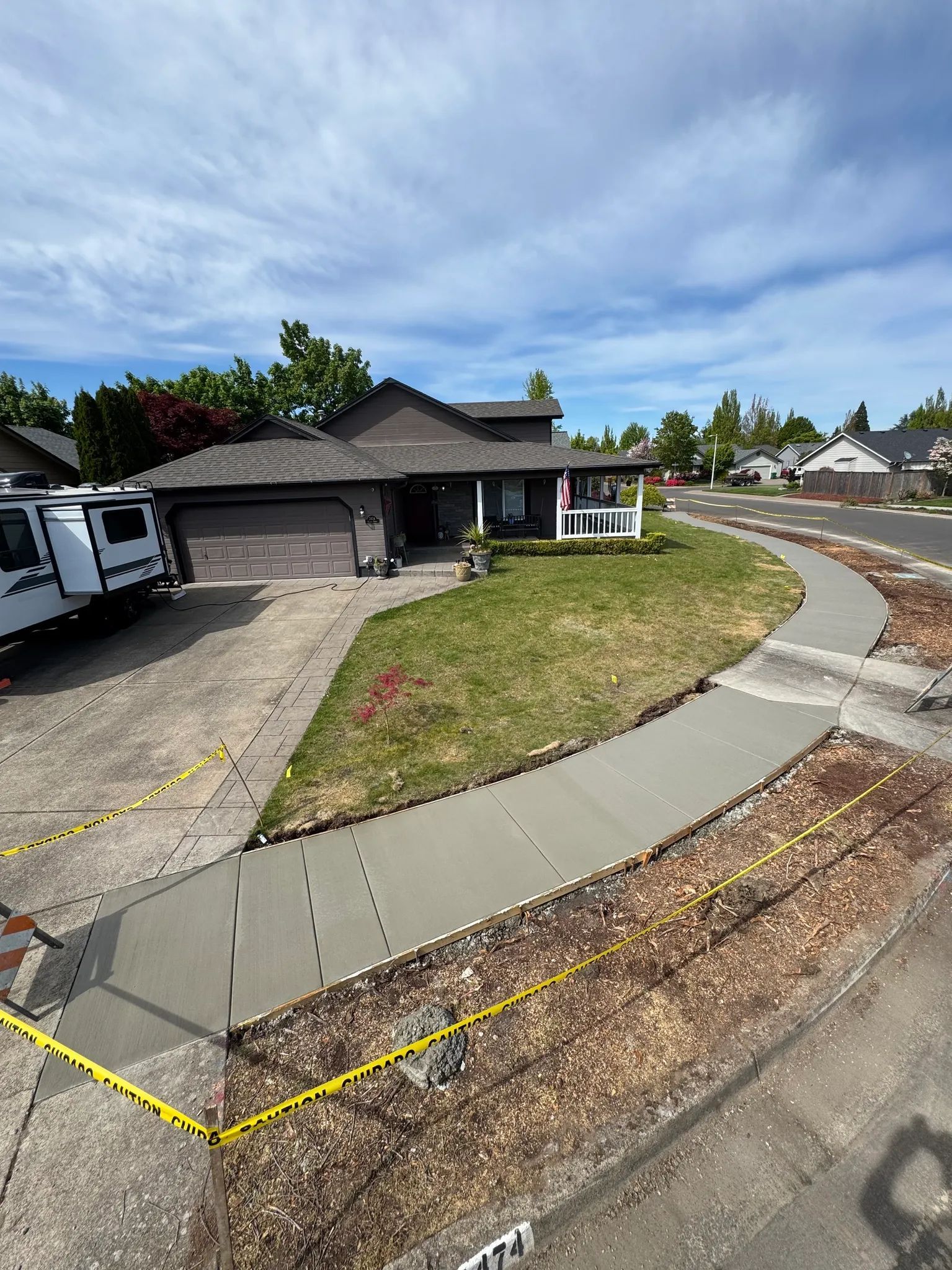 A suburban house with a newly poured concrete driveway apron and sidewalk marked with yellow caution tape.