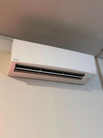 Wall-mounted white air conditioner above a beige wall with ceiling visible