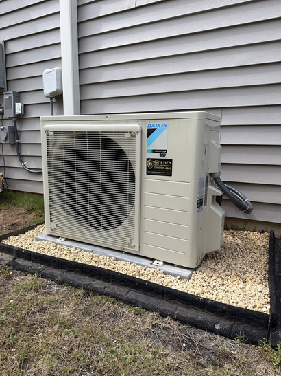 Outdoor air conditioner unit beside a house with gray siding and gravel landscaping