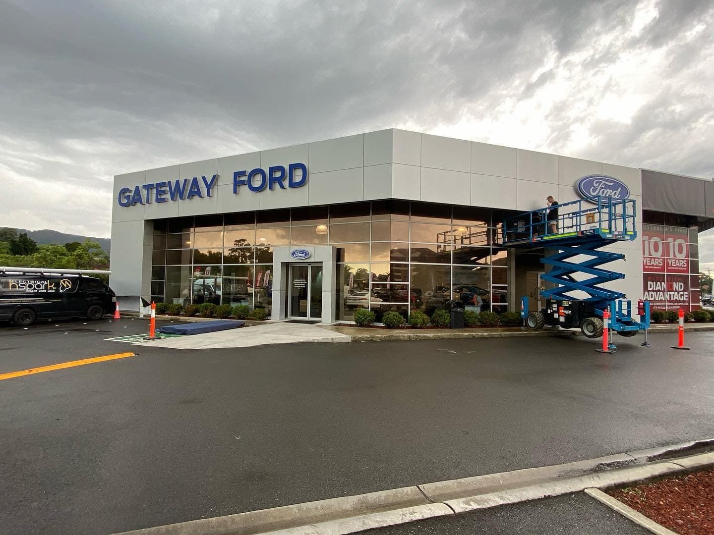 Gateway Ford Dealership With Worker in Lift Installing Sign Under Cloudy Sky — Hspark Electrical PTY LTD in Appin, NSW