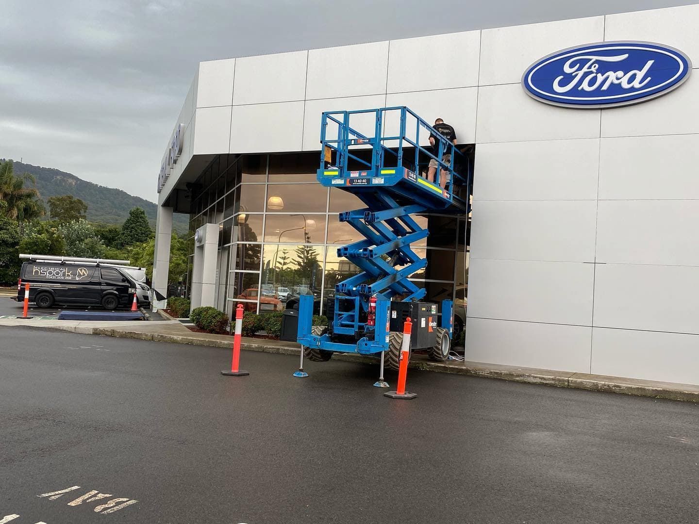 A Blue Scissor Lift at a Ford Dealership is Positioned Near a Window — Hspark Electrical PTY LTD in Woonona, NSW