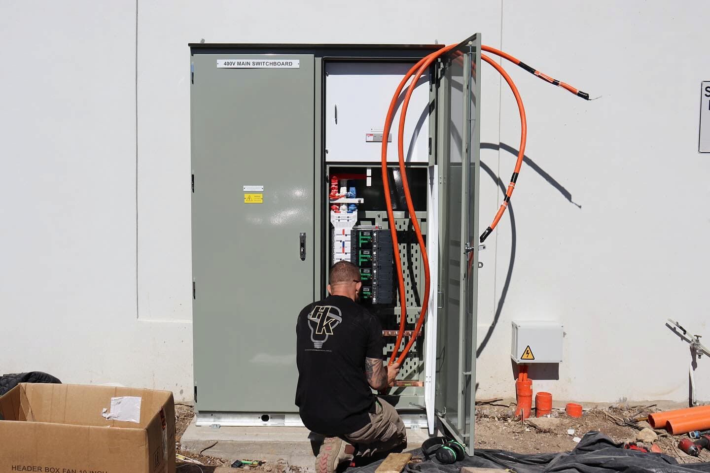 A technician works on an open industrial electrical cabinet outdoors, connected to thick orange cables — Hspark Electrical PTY LTD in Narellan, NSW