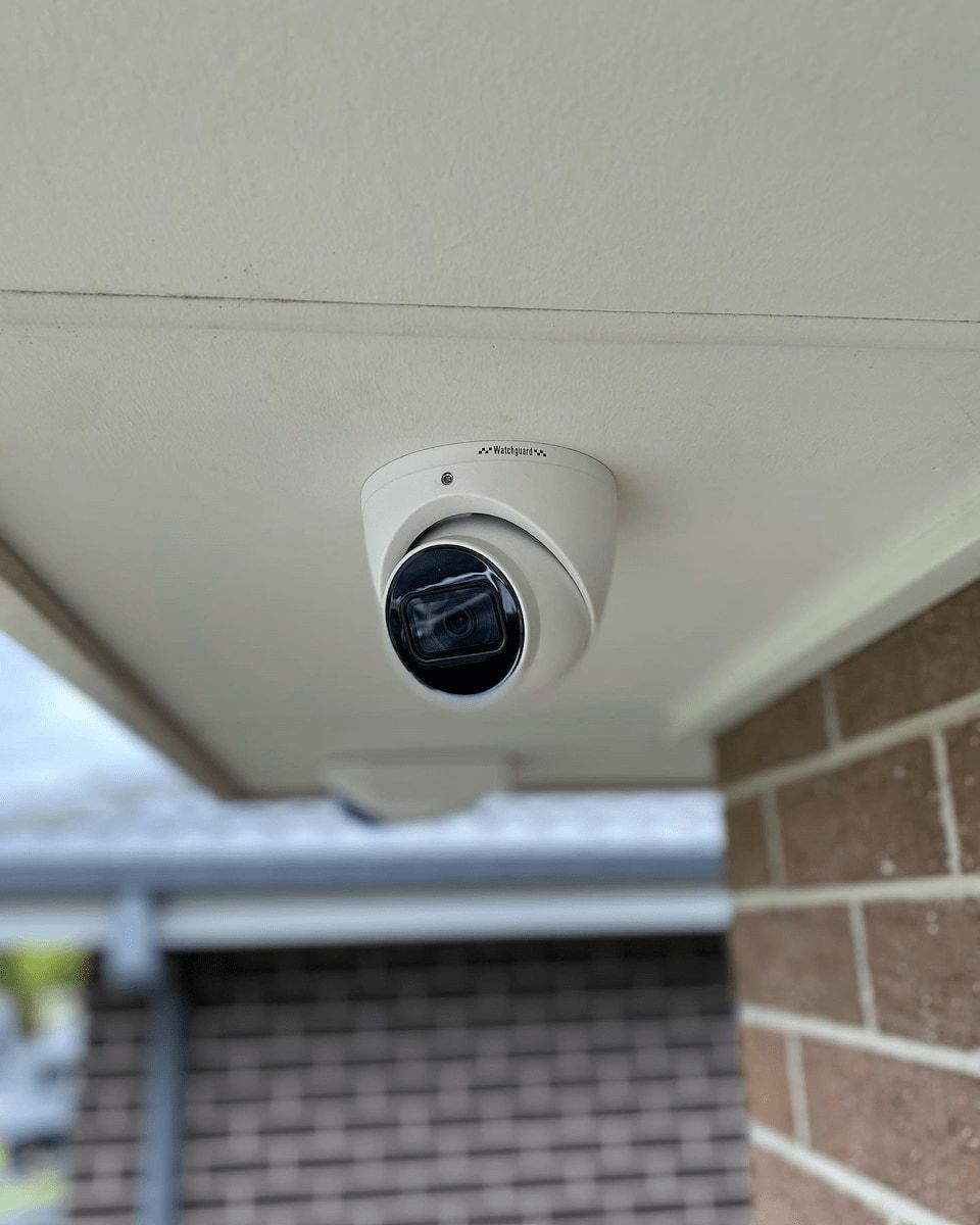 White Security Camera Mounted on a White Overhang, Brick Wall in View — Hspark Electrical PTY LTD in Appin, NSW