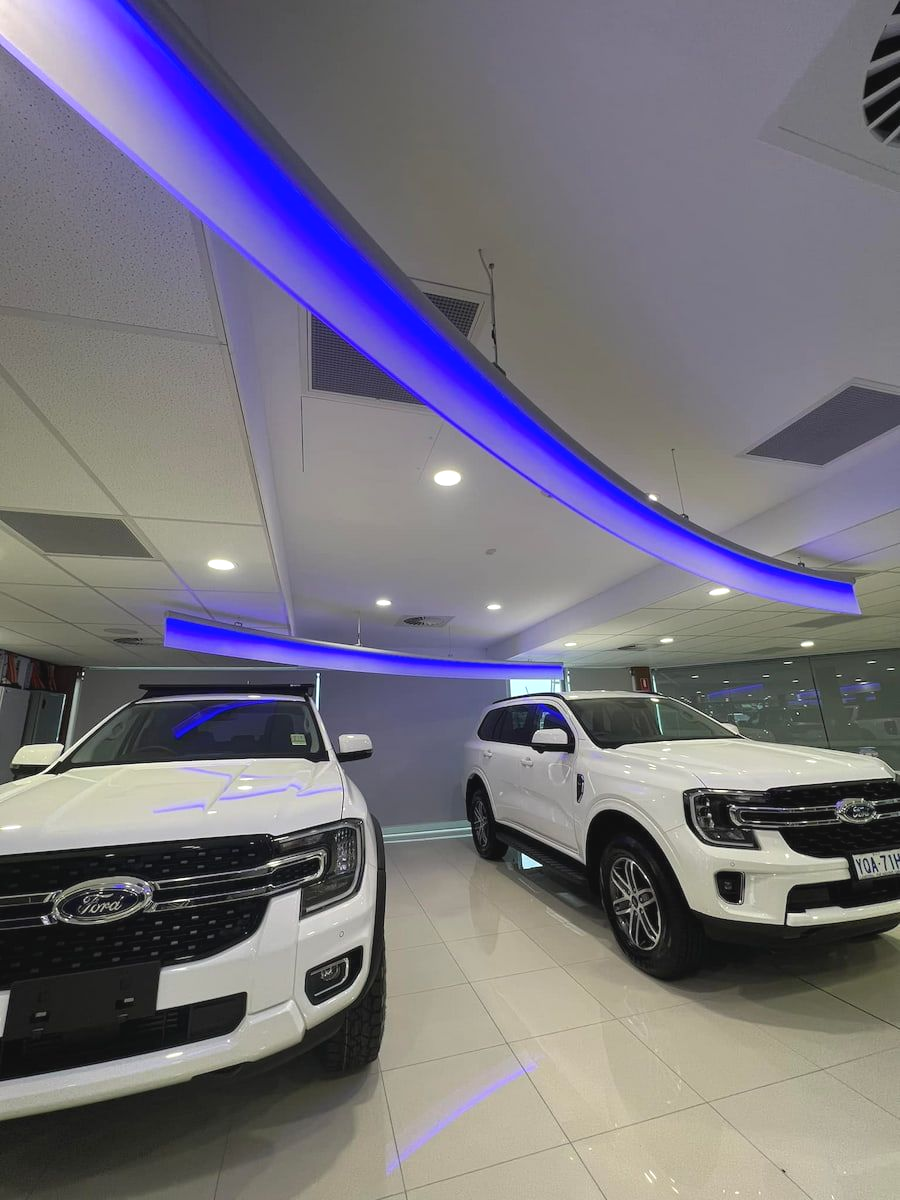 Two White Ford Everest Suvs in a Showroom With Blue Ceiling Lighting — Hspark Electrical PTY LTD in Wollongong, NSW