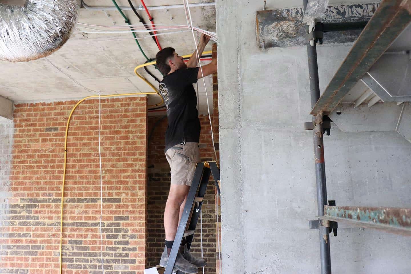 Man on Ladder Working With Wires in a Construction Setting — Hspark Electrical PTY LTD in Austinmer, NSW