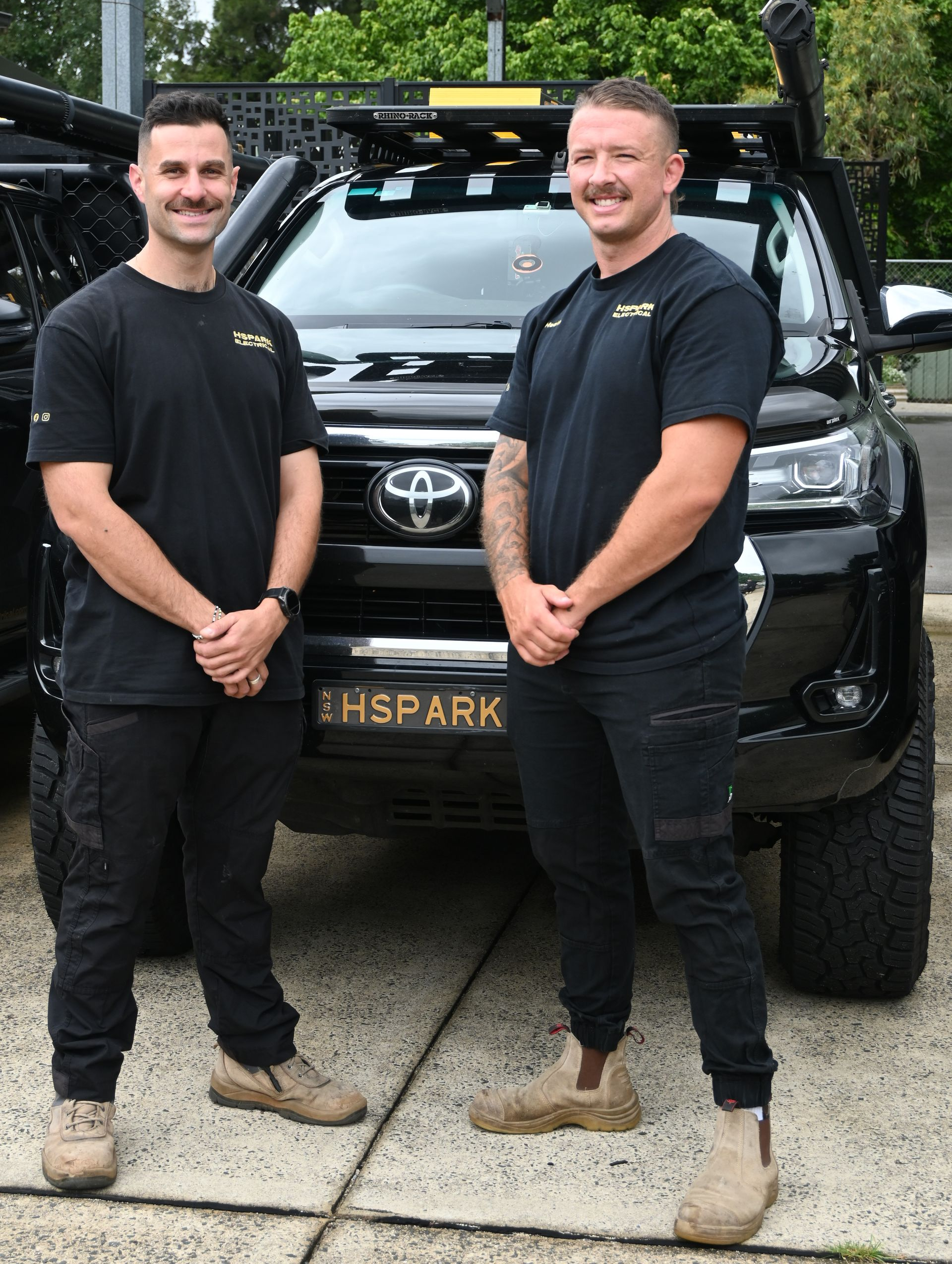 Two Men Standing Outside a Building, Looking at Equipment on the Wall — Hspark Electrical PTY LTD in Appin, NSW