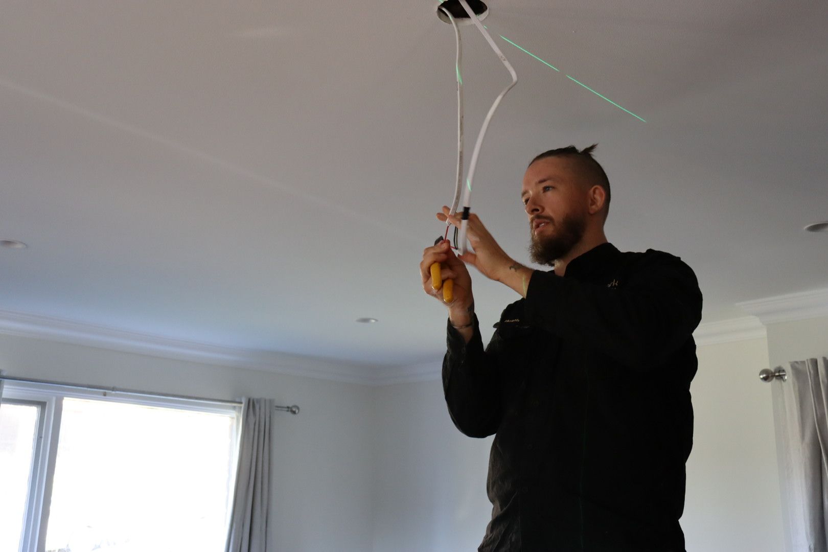 A person installs a light fixture by connecting electrical wires hanging from a ceiling in a residential room — Hspark Electrical PTY LTD in Narellan, NSW