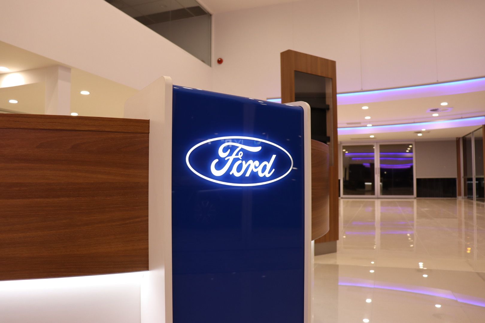 A glowing, blue, illuminated Ford logo on a reception desk in a modern, brightly lit dealership showroom — Hspark Electrical PTY LTD in Appin, NSW