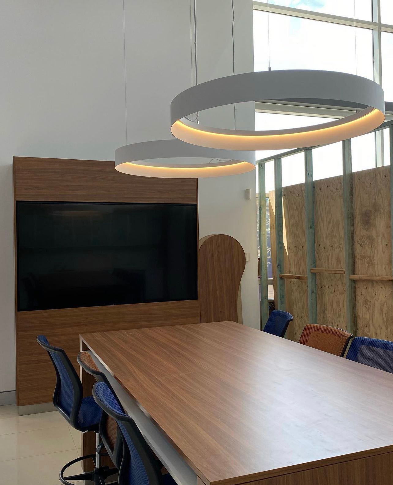 A conference room with a wooden table, blue chairs, a wall-mounted TV, and two large circular pendant lights — Hspark Electrical PTY LTD in Woonona, NSW