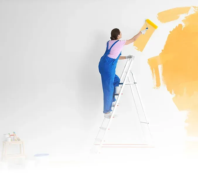 Person painting a wall yellow while standing on a ladder in a bright white room