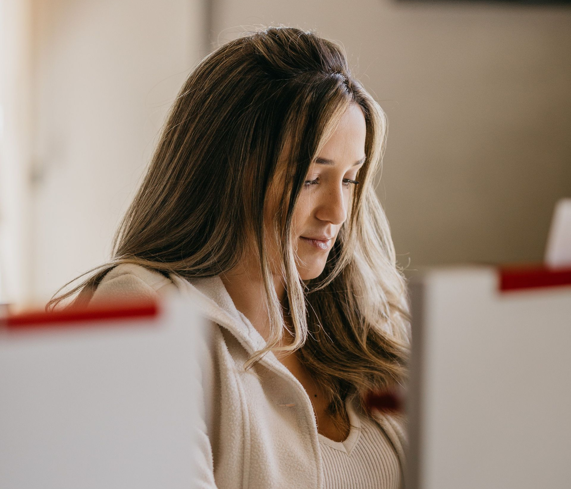 Woman with long brown hair looking down at a laptop in a bright office setting