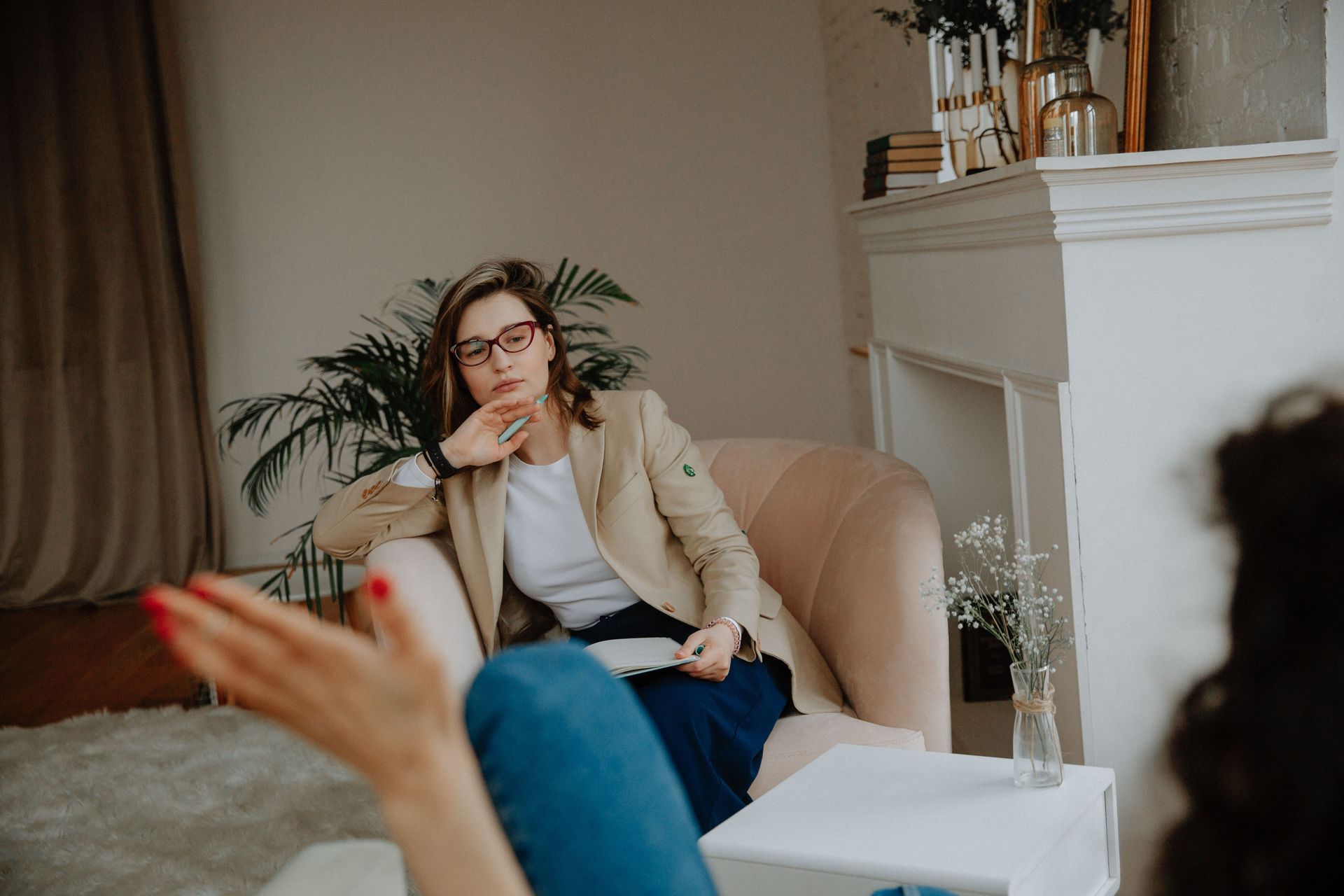 Woman in a beige blazer speaks during a seated conversation in a cozy living room.
