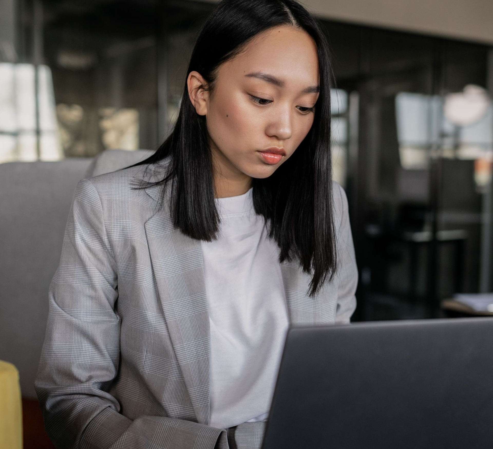 Woman with long brown hair looking down at a laptop in a bright office setting
