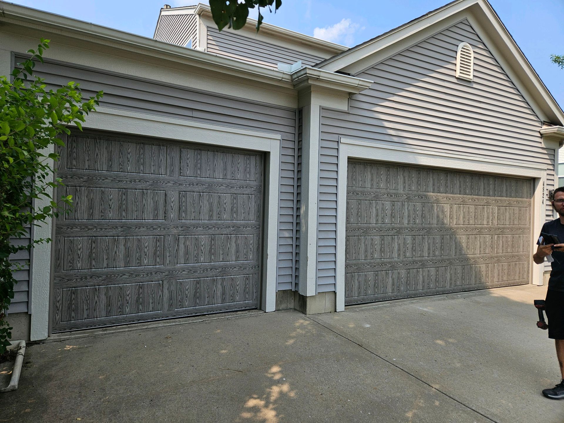 Two modern gray garage doors with a wood-grain texture and black hardware installed on a Gladstone 