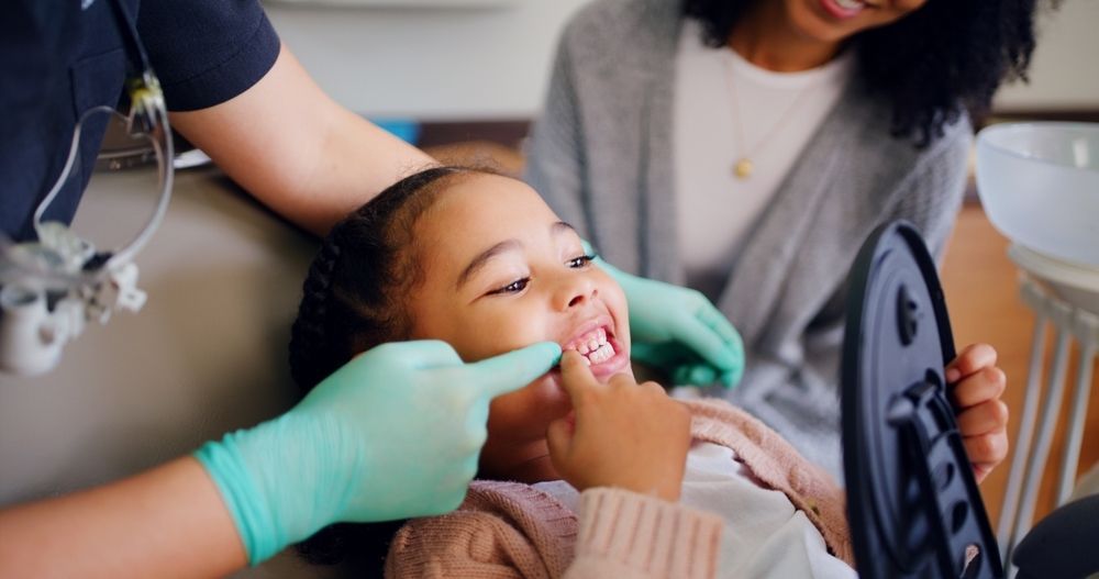 A young boy is sitting in a dental chair while a dentist examines his teeth.