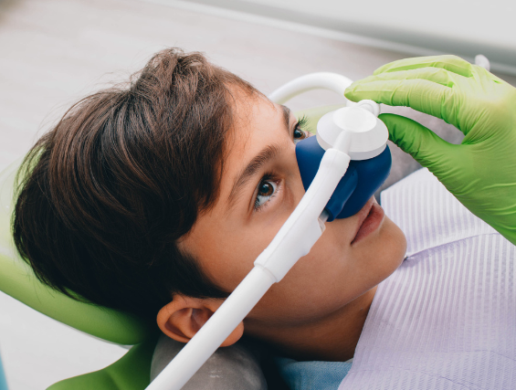 A young boy is laying in a dental chair with an oxygen mask on his face.