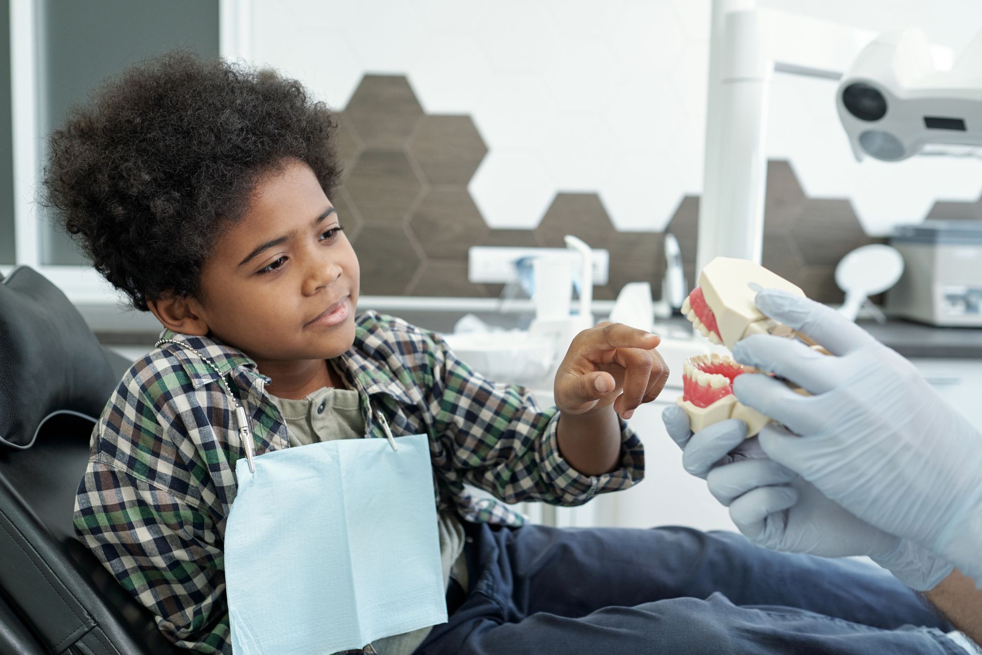 A young boy is sitting in a dental chair looking at a model of teeth. Restorative dental care near Tarrytown, NY