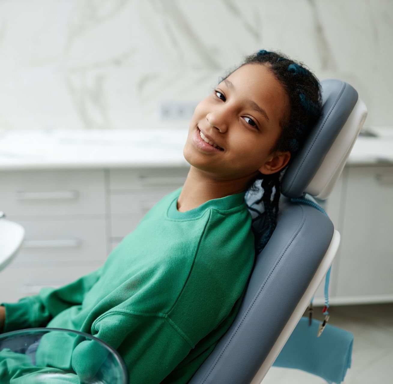 A young girl in a green shirt is sitting in a dental chair after a dental filling in Tarrytown, NY