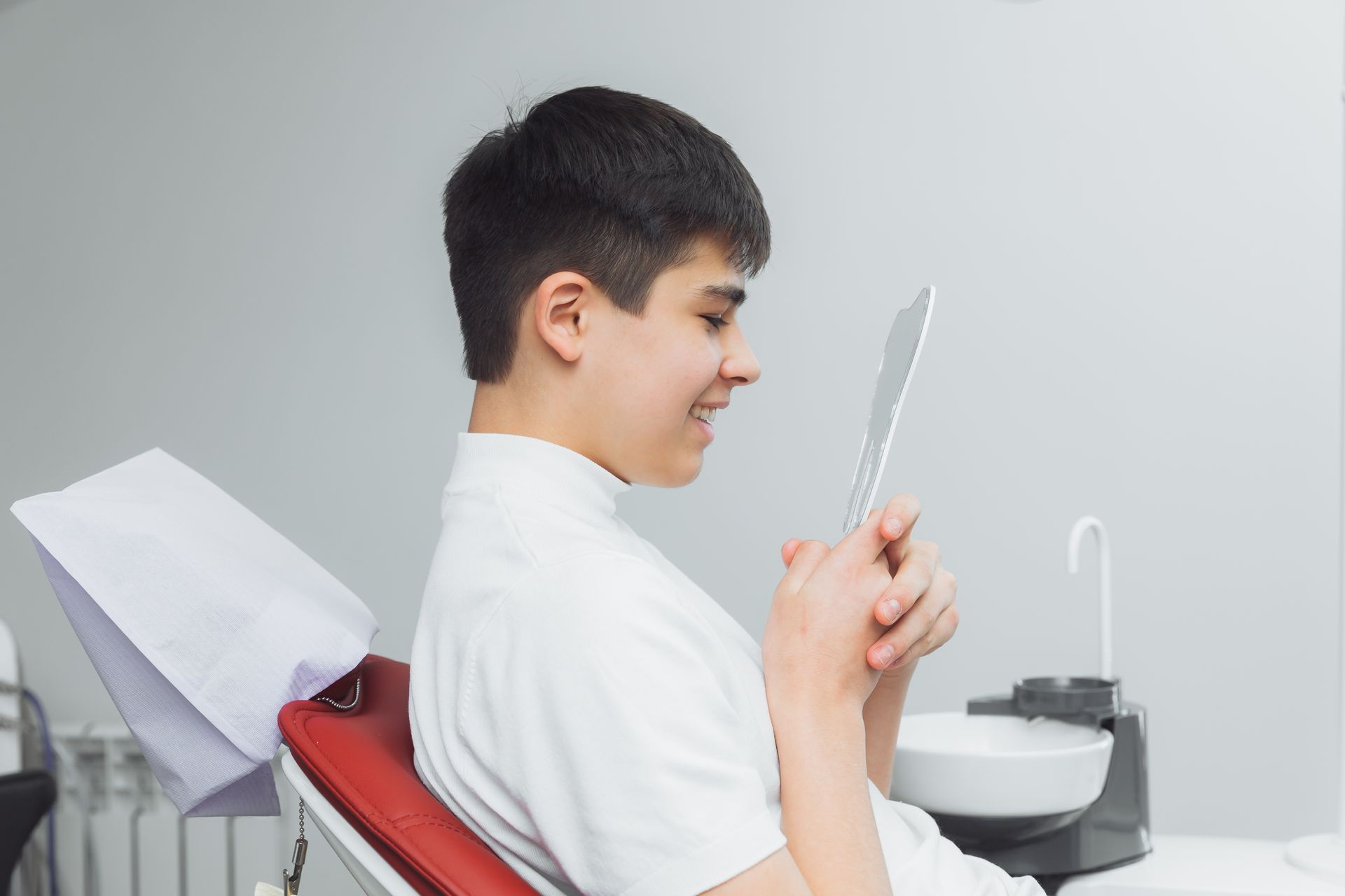 A young boy is sitting in a dental chair looking at his teeth in a mirror, non-invasive dental treatments in Tarrytown, NY